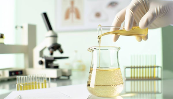 gold colored oil pouring into a beaker with a lab background